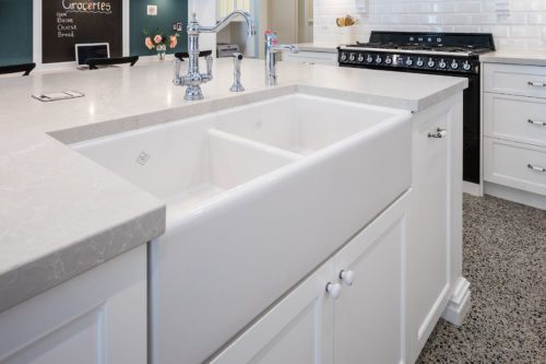 A white kitchen sink built into the side of custom kitchen cabinets on an island bench