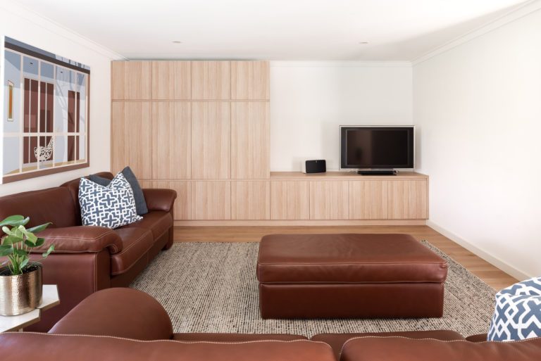 A lounge room with a brown couch and wooden cabinets