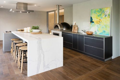 Kitchen with dark custom cabinets and a marble white island bench